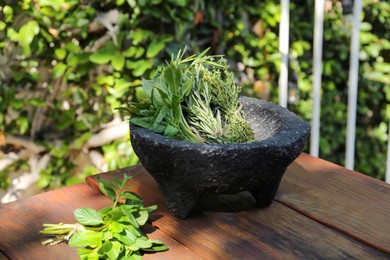 Mortar with thyme, rosemary and basil on wooden table outdoors. Aromatic herbs