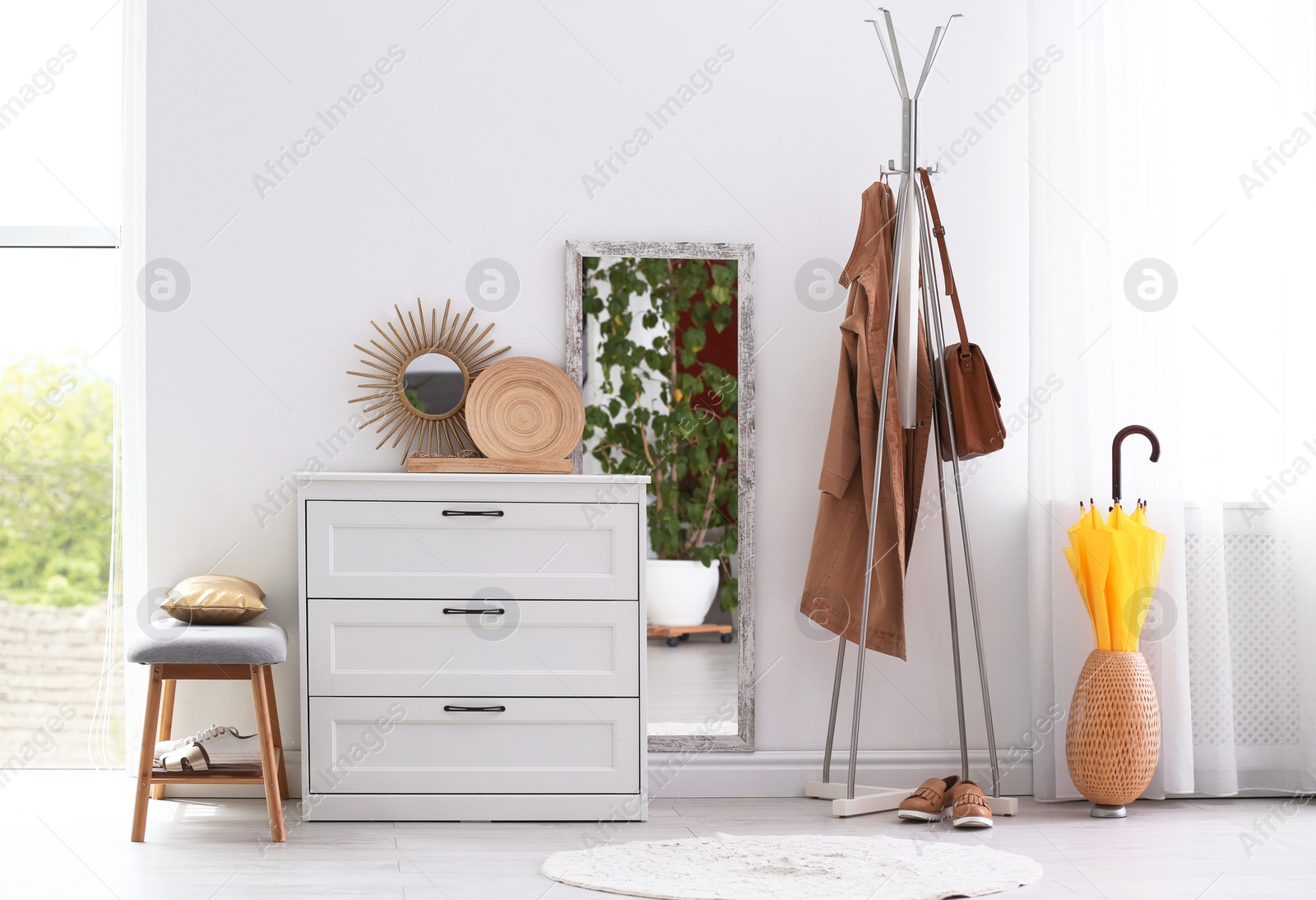 Photo of Modern hallway interior with chest of drawers and clothes on hanger stand. Space for text