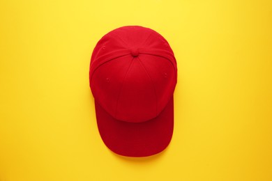 Photo of Stylish red baseball cap on yellow background, top view