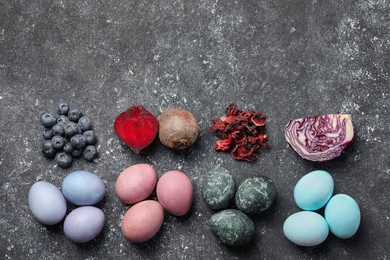 Painted Easter eggs with natural organic dyes (blueberries, beetroot, hibiscus, and red cabbage) on black table, flat lay. Space for text