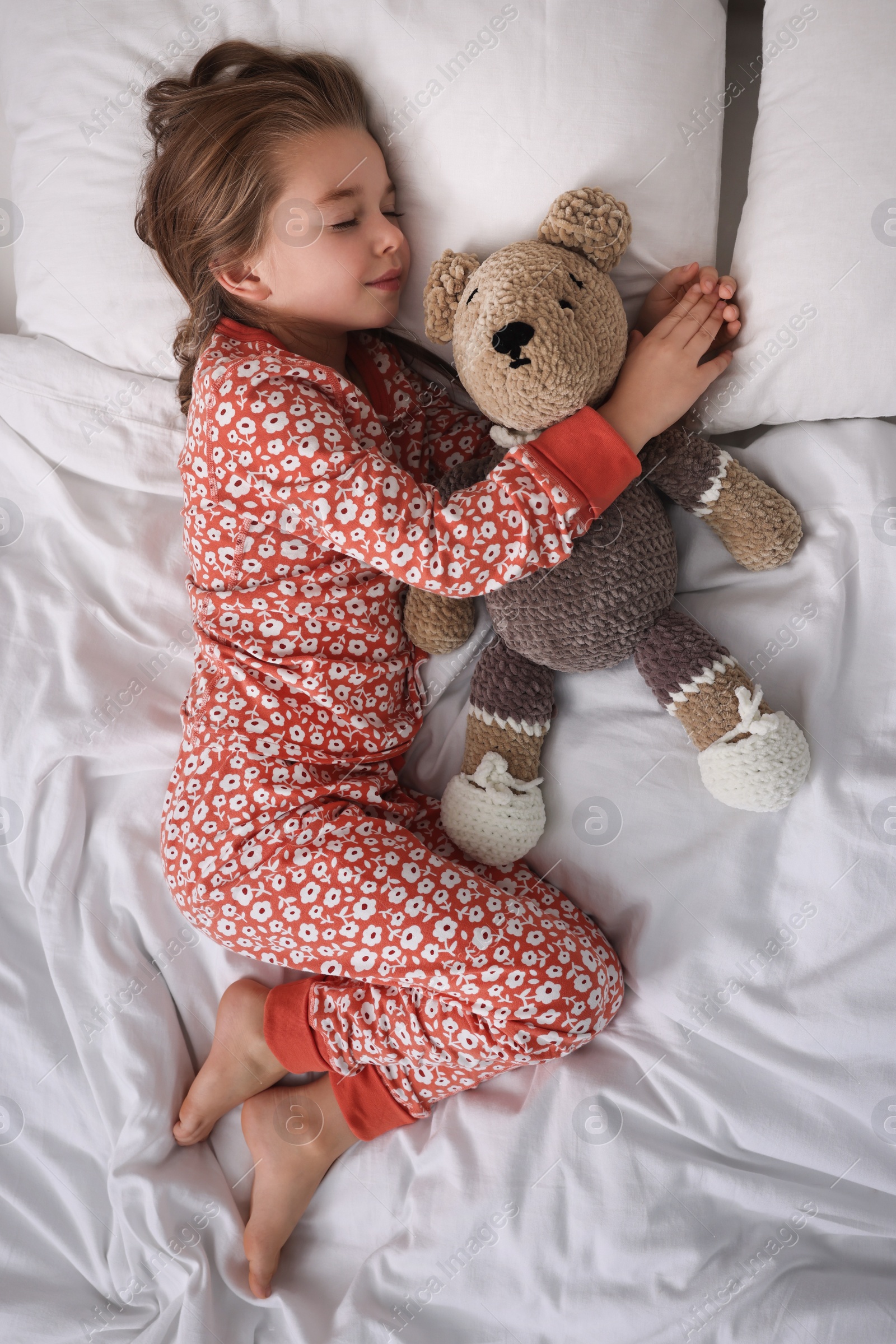 Photo of Cute little girl with toy bear sleeping on bed, top view
