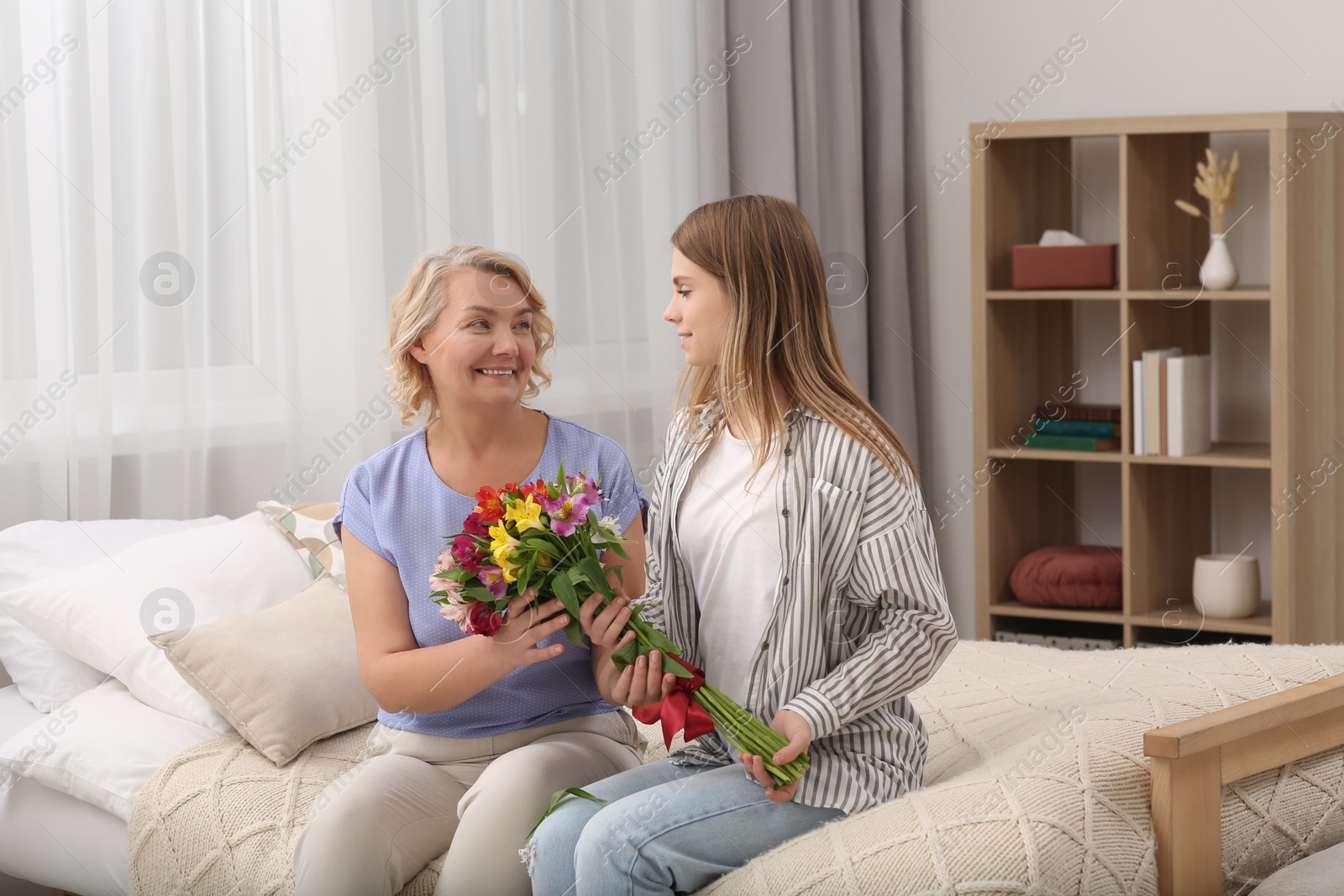 Photo of Young daughter congratulating her mom with flowers at home. Happy Mother's Day