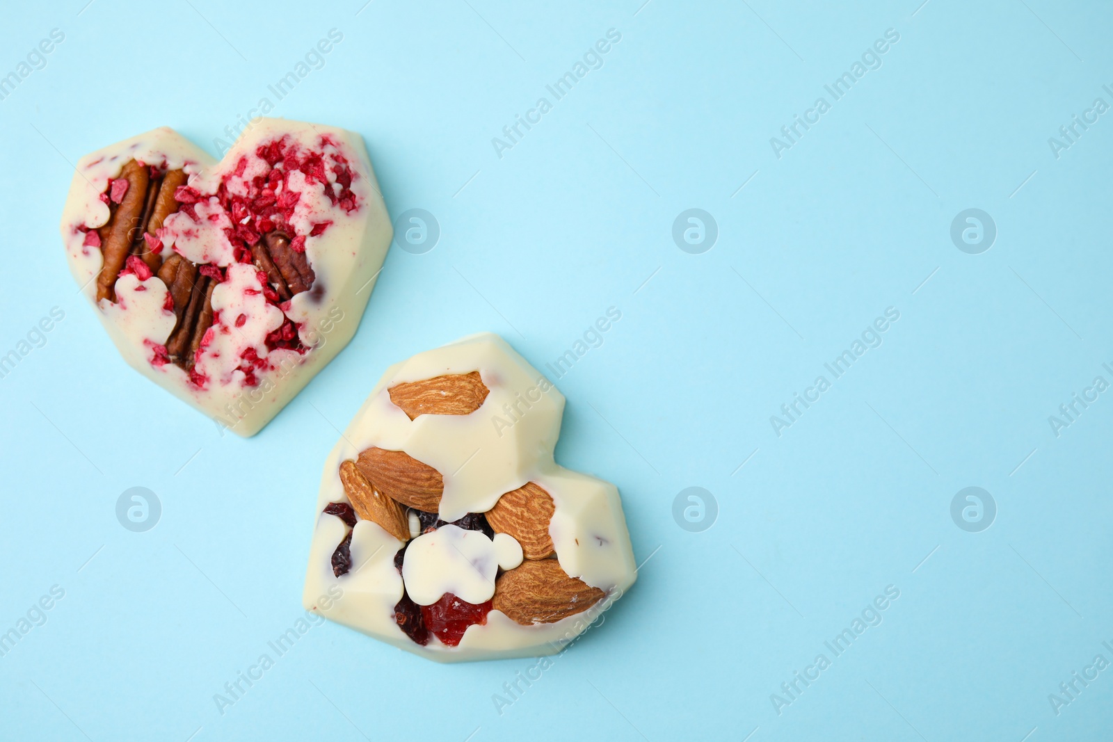 Photo of Tasty chocolate heart shaped candies with nuts on light blue background, flat lay. Space for text