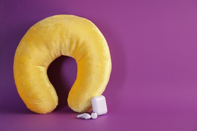 Photo of Yellow travel pillow and earphones on violet background, space for text