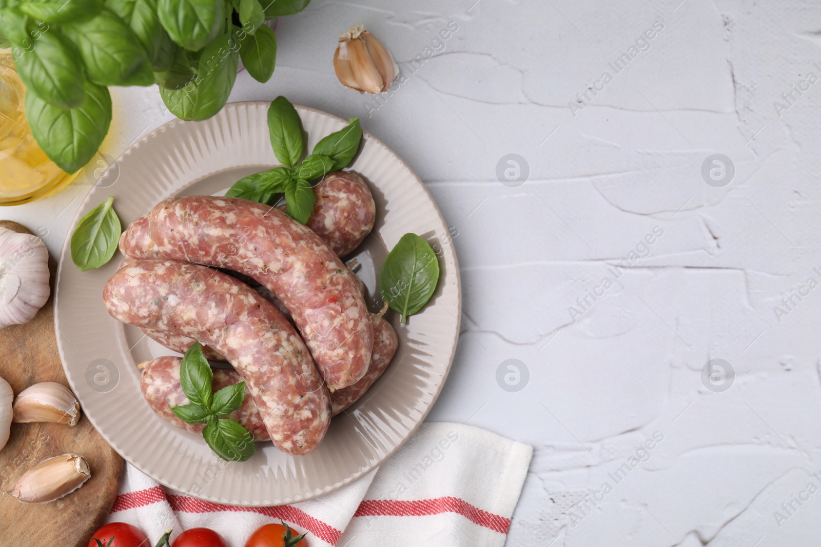 Photo of Raw homemade sausages and different products on white textured table, flat lay. Space for text