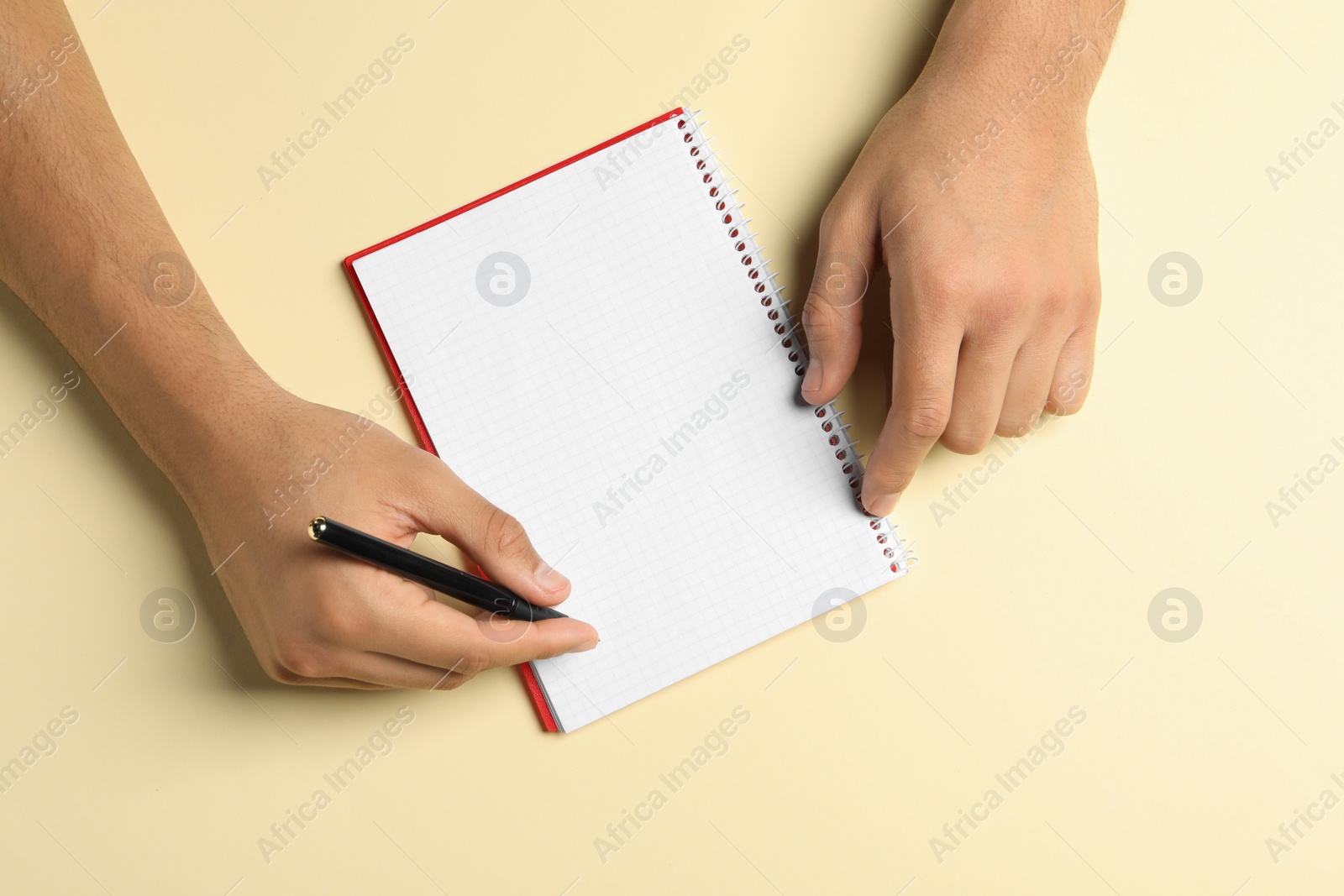Photo of Man with pen and notepad on pale yellow background, top view