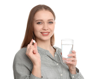 Young woman with glass of water and vitamin pill on white background