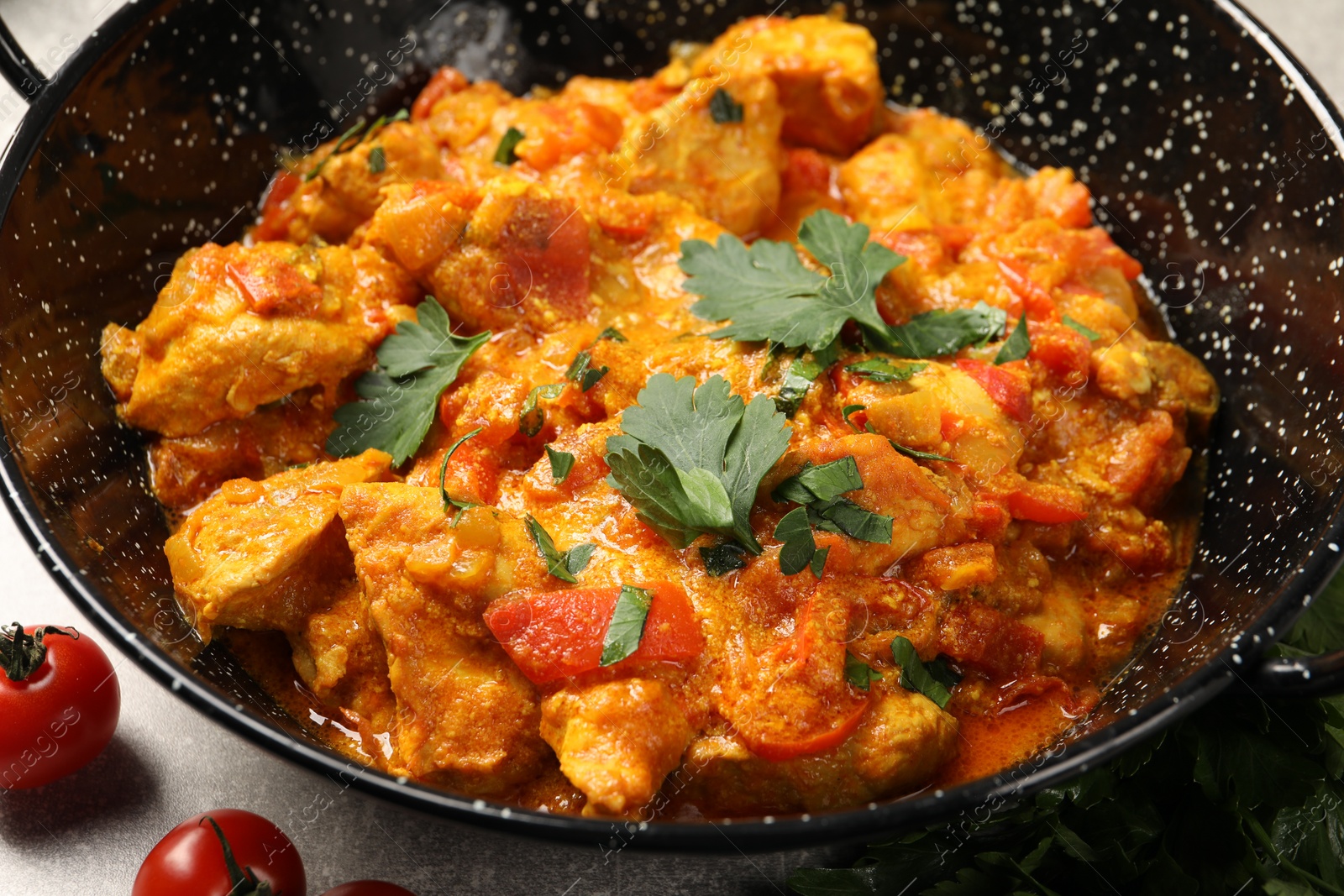 Photo of Delicious chicken curry in frying pan and tomatoes on table, closeup