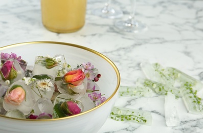 Photo of Bowl and floral ice cubes on table, closeup. Space for text