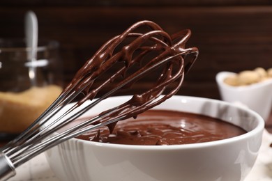 Photo of Bowl and whisk with chocolate cream on table, closeup