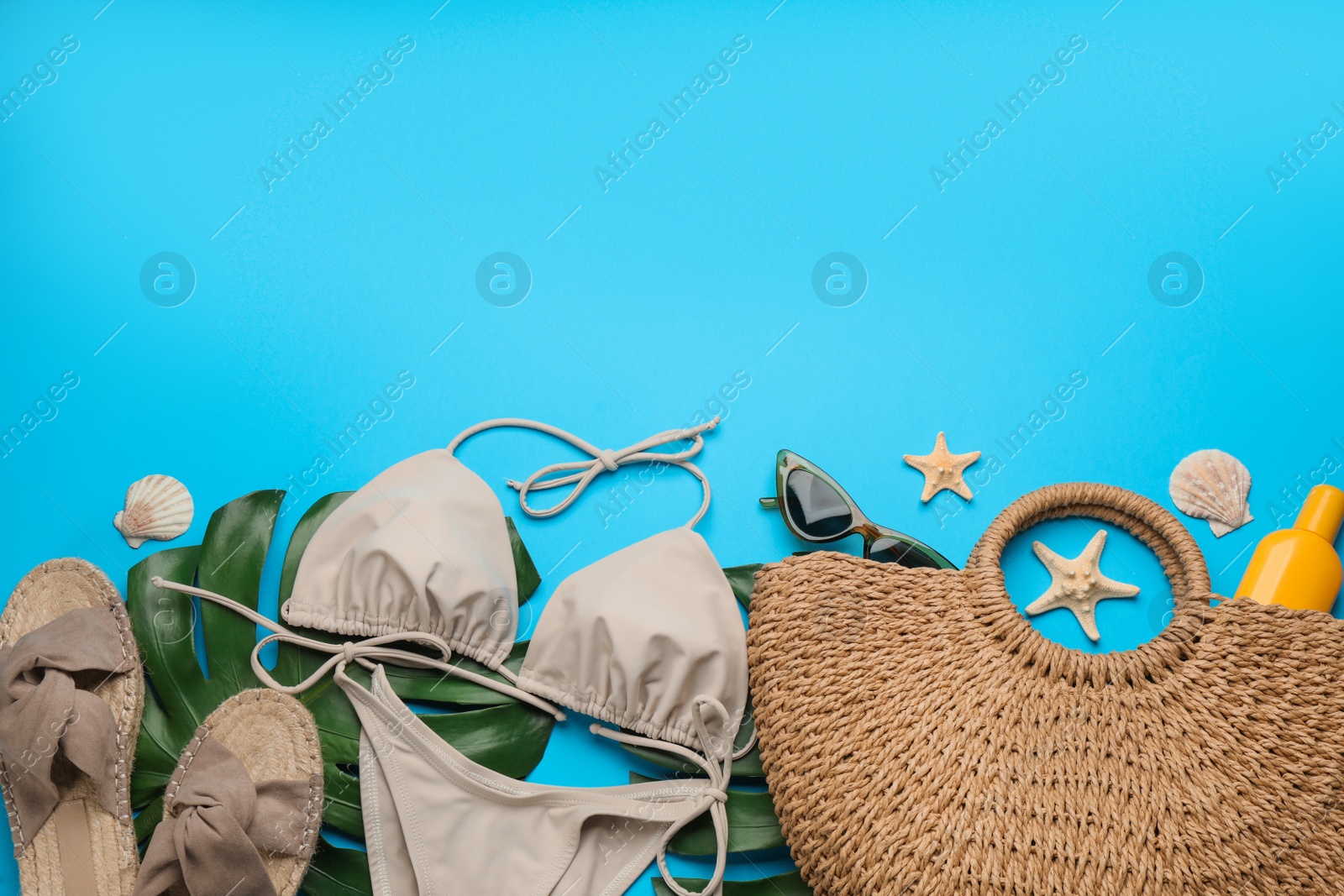 Photo of Stylish bag with beach accessories on light blue background, flat lay. Space for text