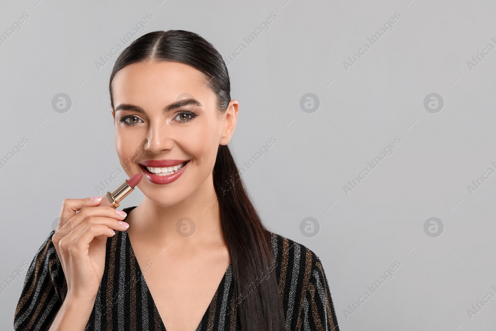 Photo of Everyday makeup. Beautiful woman applying lipstick on light grey background, space for text