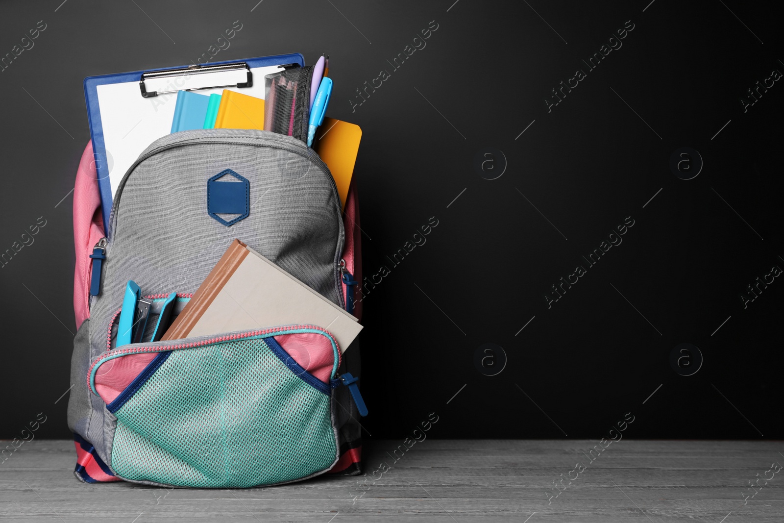 Photo of Backpack with different school stationery on grey wooden table near blackboard, space for text