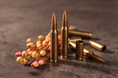 Photo of Bullets and beautiful dry plant on grey textured table, closeup