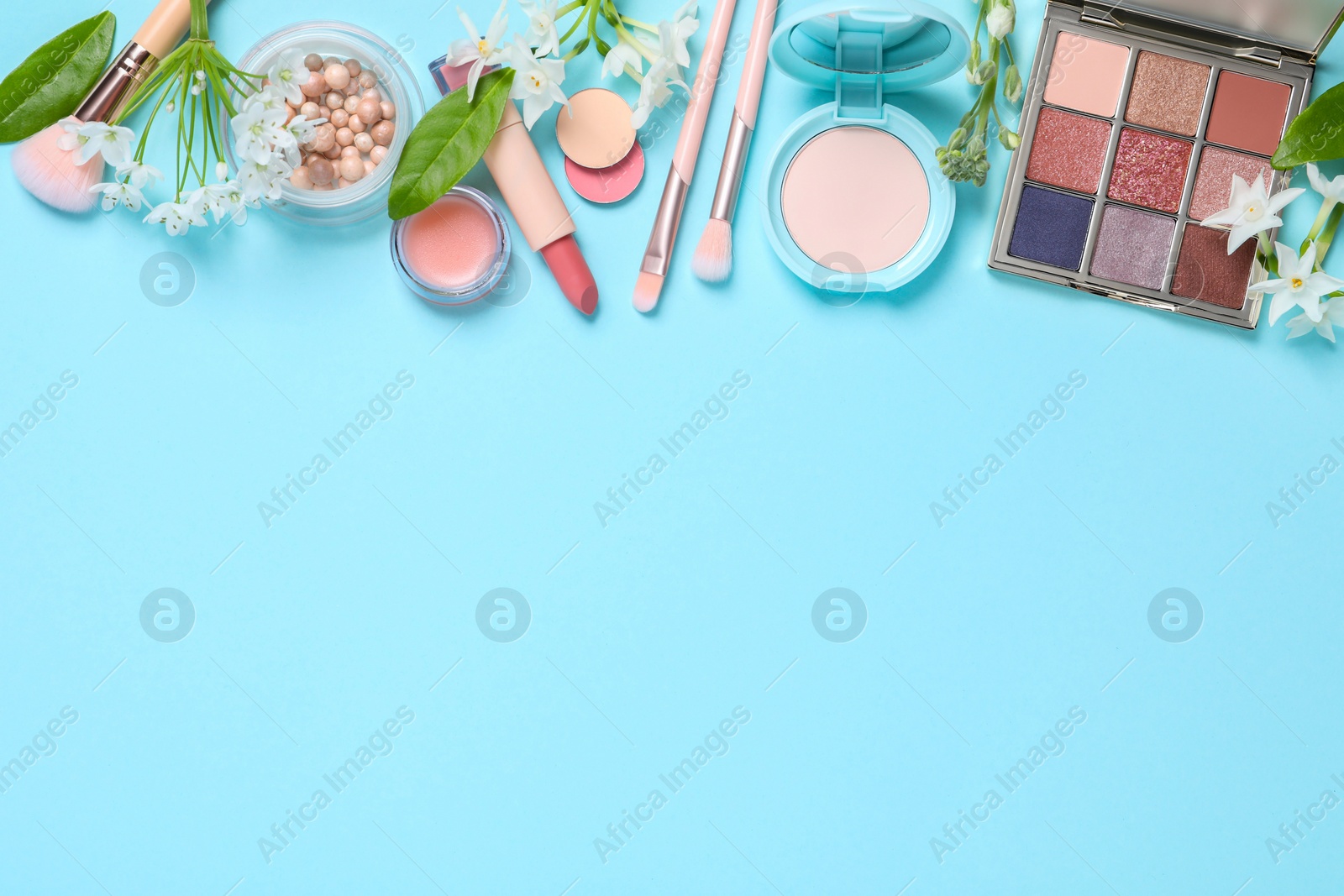 Photo of Flat lay composition with eyeshadow palette and beautiful flowers on light blue background, space for text