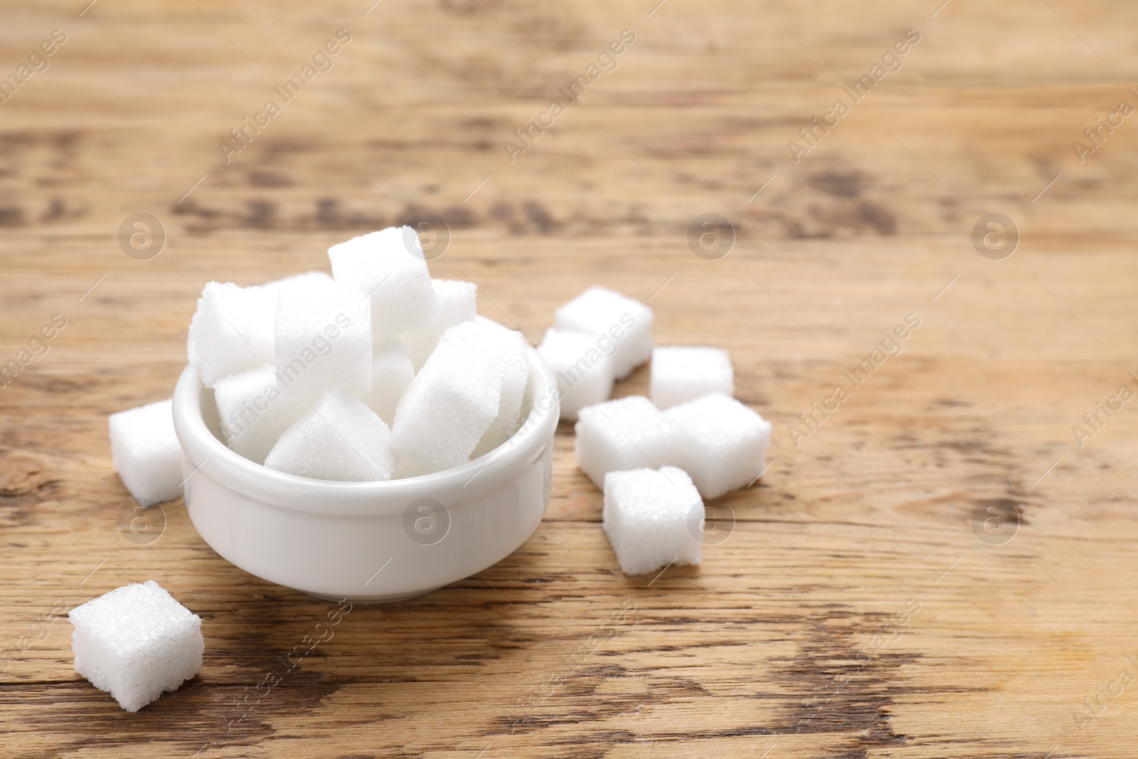 Photo of White sugar cubes on wooden table, space for text