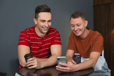 Men with cups of coffee and smartphone laughing together at table indoors