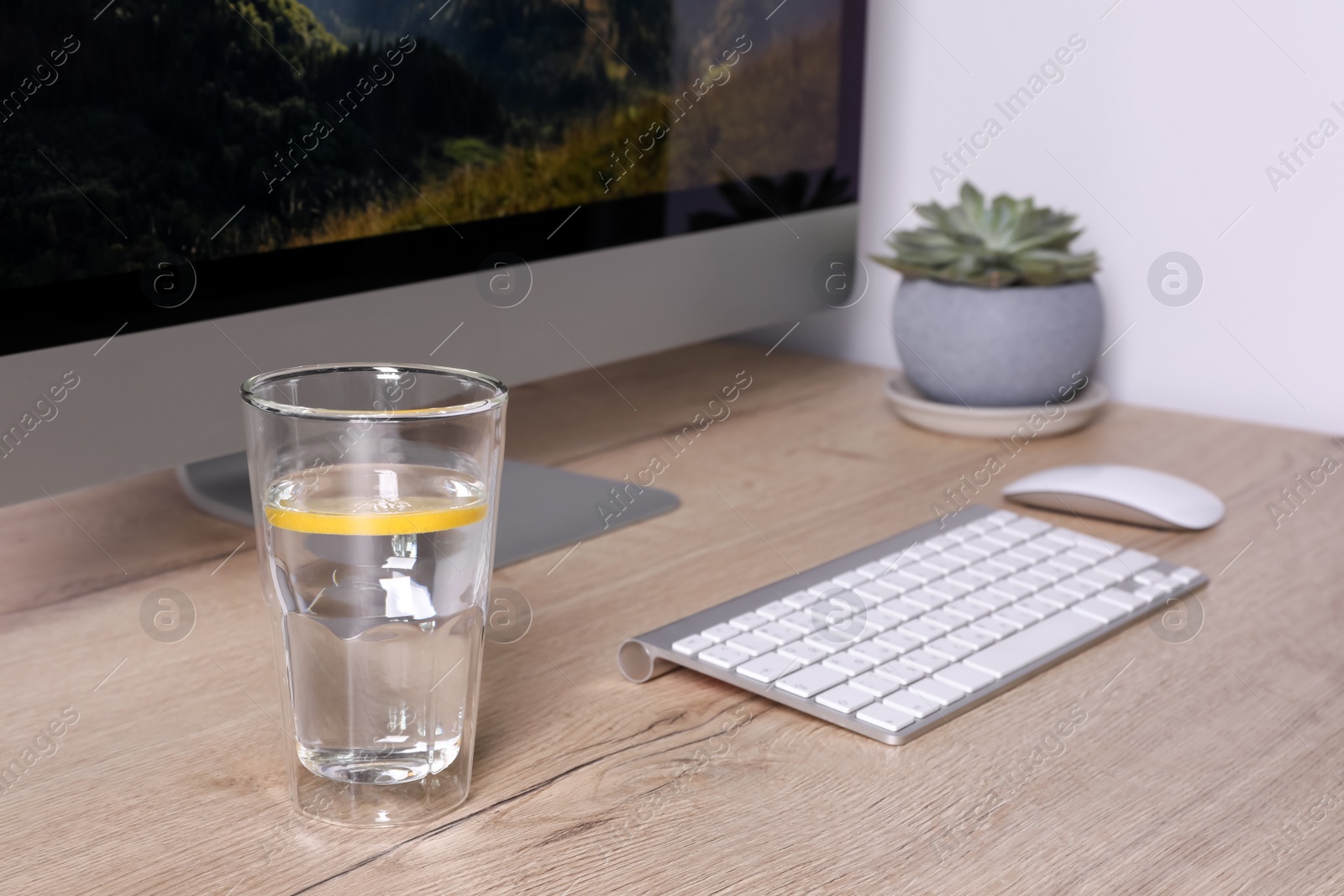 Photo of Glass of lemon water and modern computer on wooden table indoors