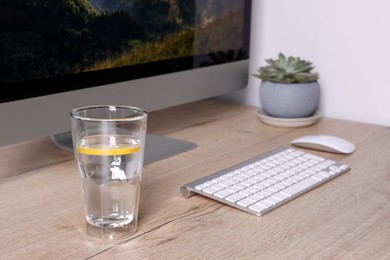 Photo of Glass of lemon water and modern computer on wooden table indoors