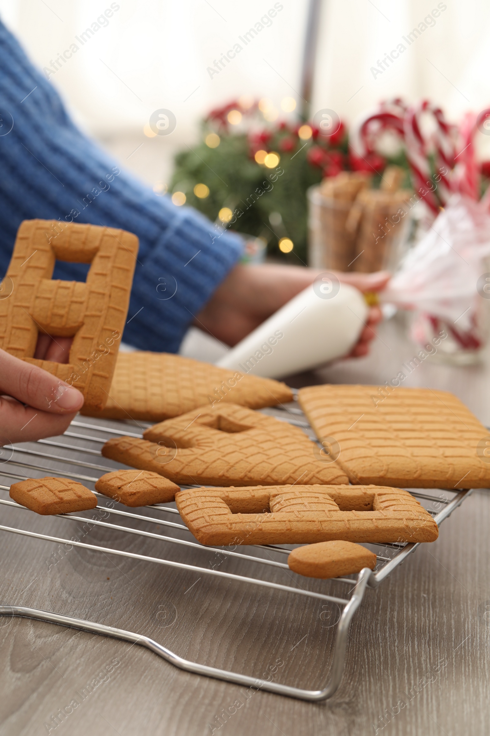 Photo of Woman making gingerbread house at wooden table, closeup