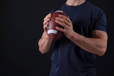 Photo of Athletic man with American football ball on black background, closeup. Space for text