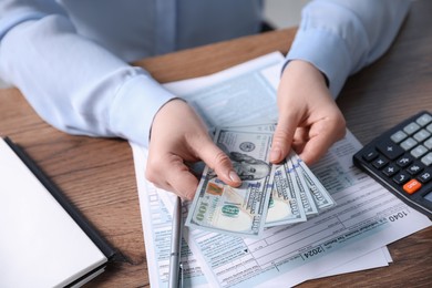 Photo of Payroll. Woman with dollar banknotes and tax return forms at wooden table, closeup