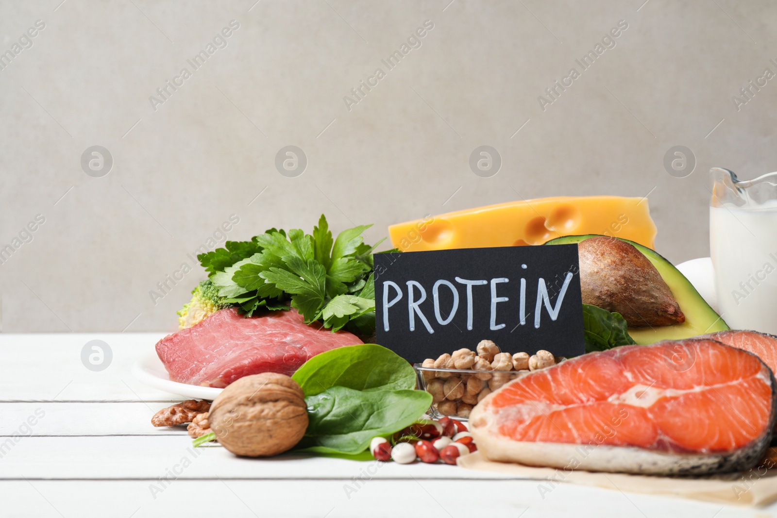 Photo of Card with word PROTEIN and different products on white wooden table