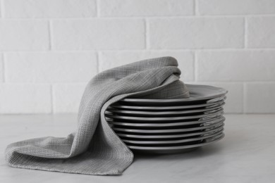 Photo of Clean grey kitchen towel and stack of plates on light table near white brick wall