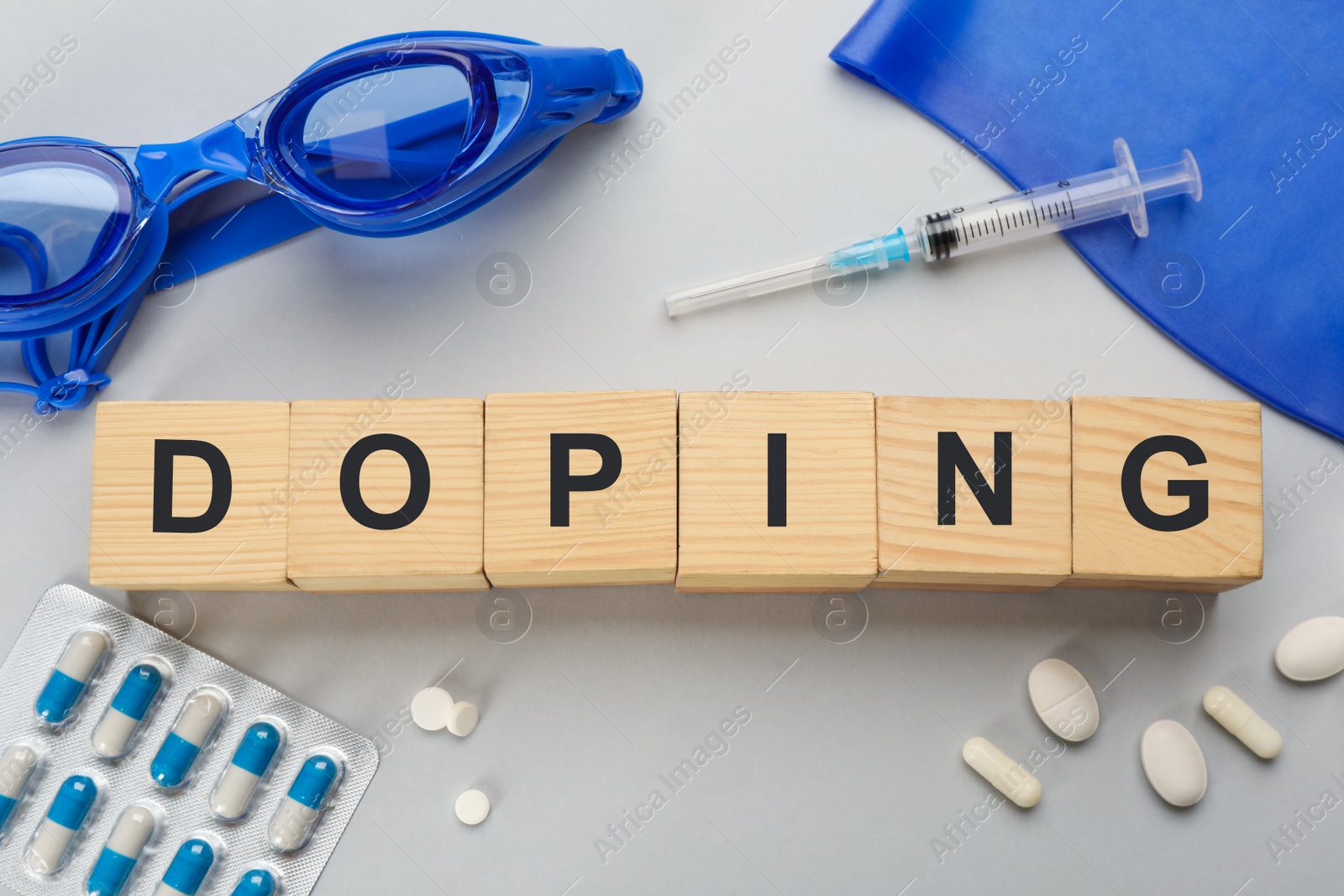 Photo of Wooden cubes with word Doping, drugs, swimming goggles and cap on light grey background, flat lay