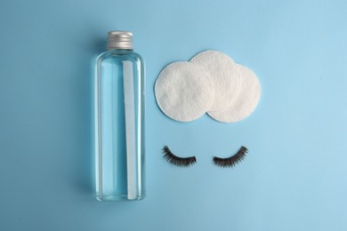 Bottle of makeup remover, cotton pads and false eyelashes on light blue background, flat lay