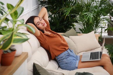 Photo of Beautiful woman resting on sofa in living room decorated with houseplants. Interior design