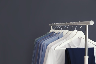 Photo of Wardrobe rack with men's clothes against grey background. Space for text