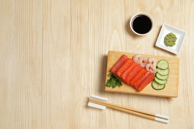 Photo of Delicious sashimi set of salmon and shrimps served with cucumbers, parsley, wasabi and soy sauce on wooden table, flat lay. Space for text
