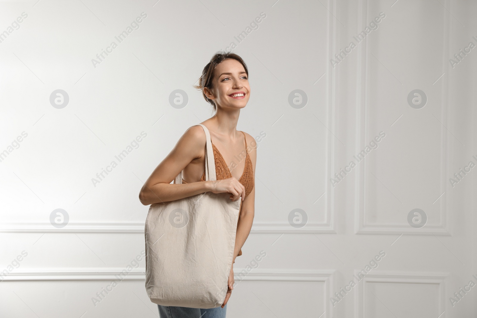 Photo of Happy young woman with blank eco friendly bag near white wall. Space for text