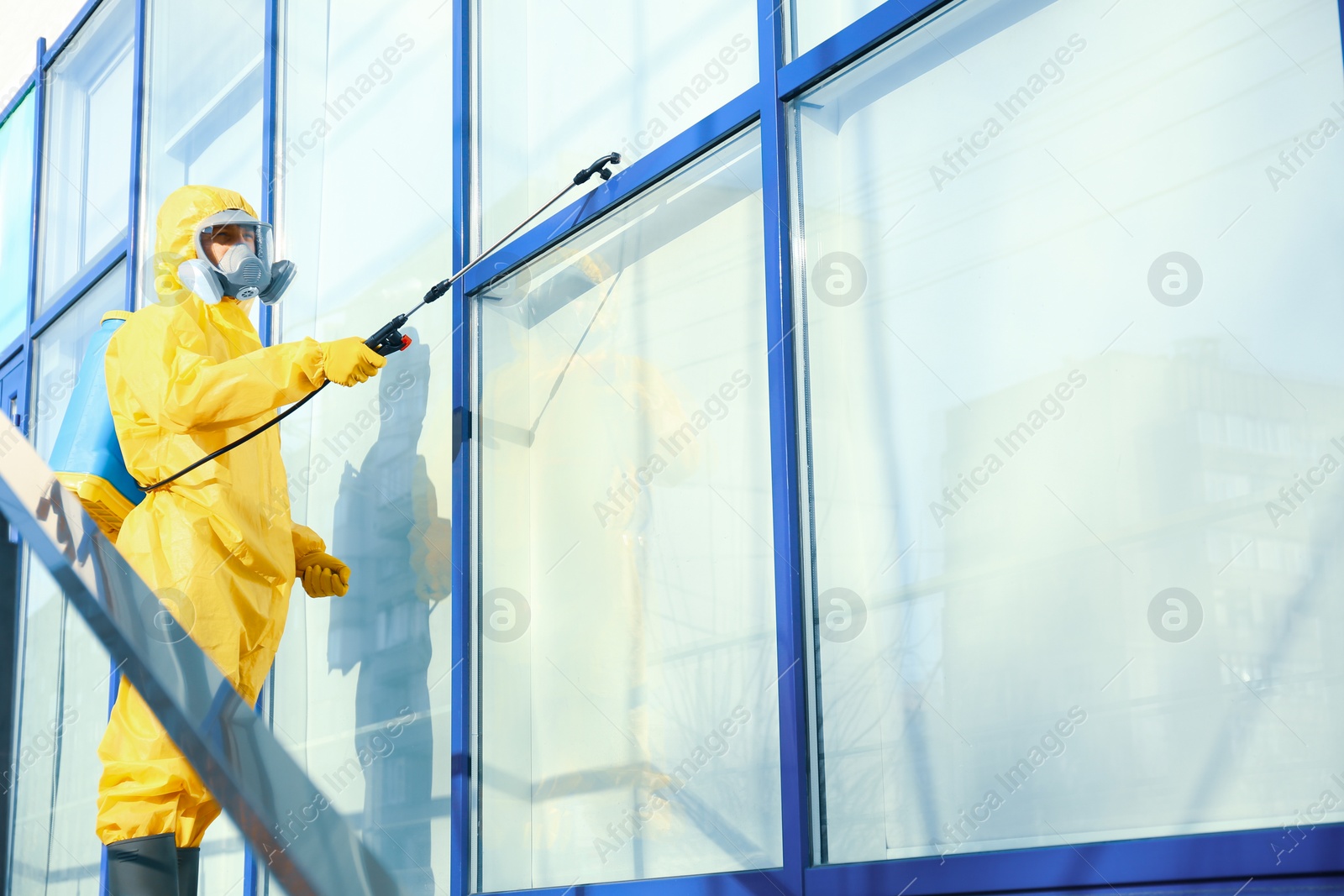 Photo of Male worker in protective suit spraying insecticide on window outdoors, space for text. Pest control