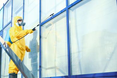 Photo of Male worker in protective suit spraying insecticide on window outdoors, space for text. Pest control
