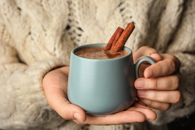 Photo of Woman holding cup of delicious hot cocoa with cinnamon, closeup