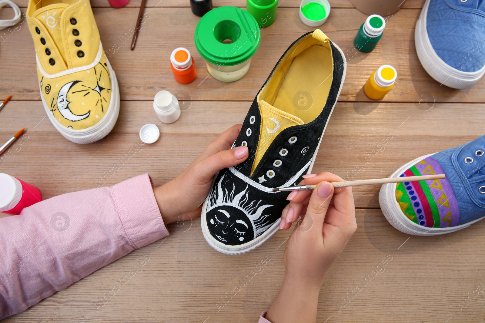 Photo of Woman painting on sneaker at wooden table, closeup. Customized shoes