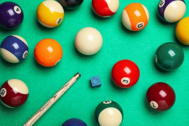 Photo of Set of billiard balls with cue and chalk on green table, flat lay