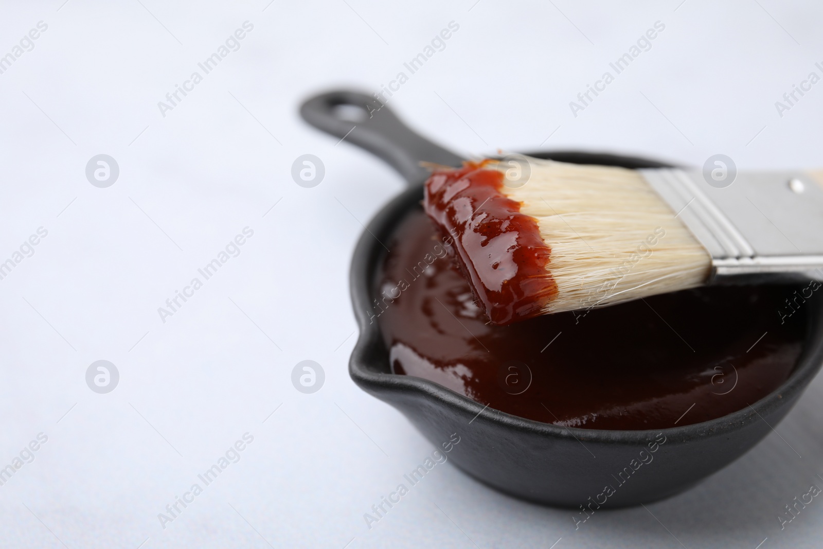 Photo of Marinade in gravy boat and basting brush on white table, closeup. Space for text
