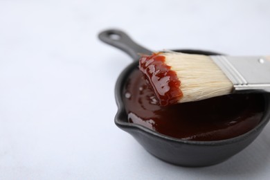 Photo of Marinade in gravy boat and basting brush on white table, closeup. Space for text