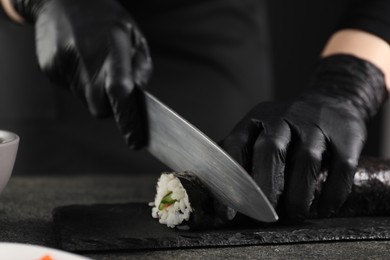 Chef in gloves cutting sushi roll at dark textured table, closeup