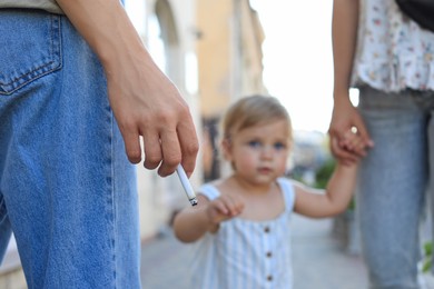 Photo of Woman smoking cigarette in public place outdoors, closeup. Don't smoke near kids