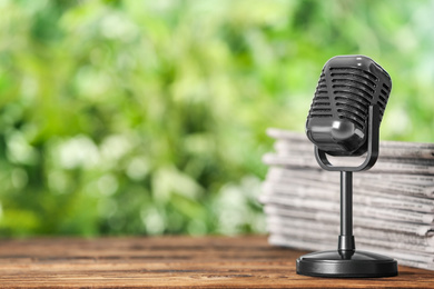 Photo of Newspapers and vintage microphone on wooden table against blurred green background, space for text. Journalist's work