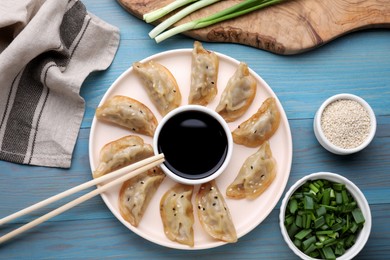 Photo of Delicious gyoza (asian dumplings) with green onions and soy sauce served on light blue wooden table, flat lay