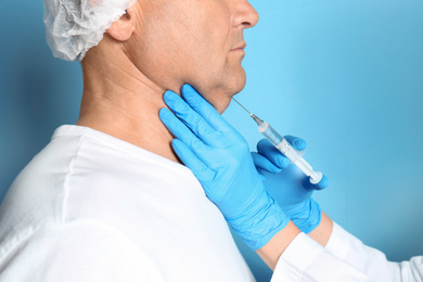 Photo of Mature man with double chin receiving injection on blue background, closeup