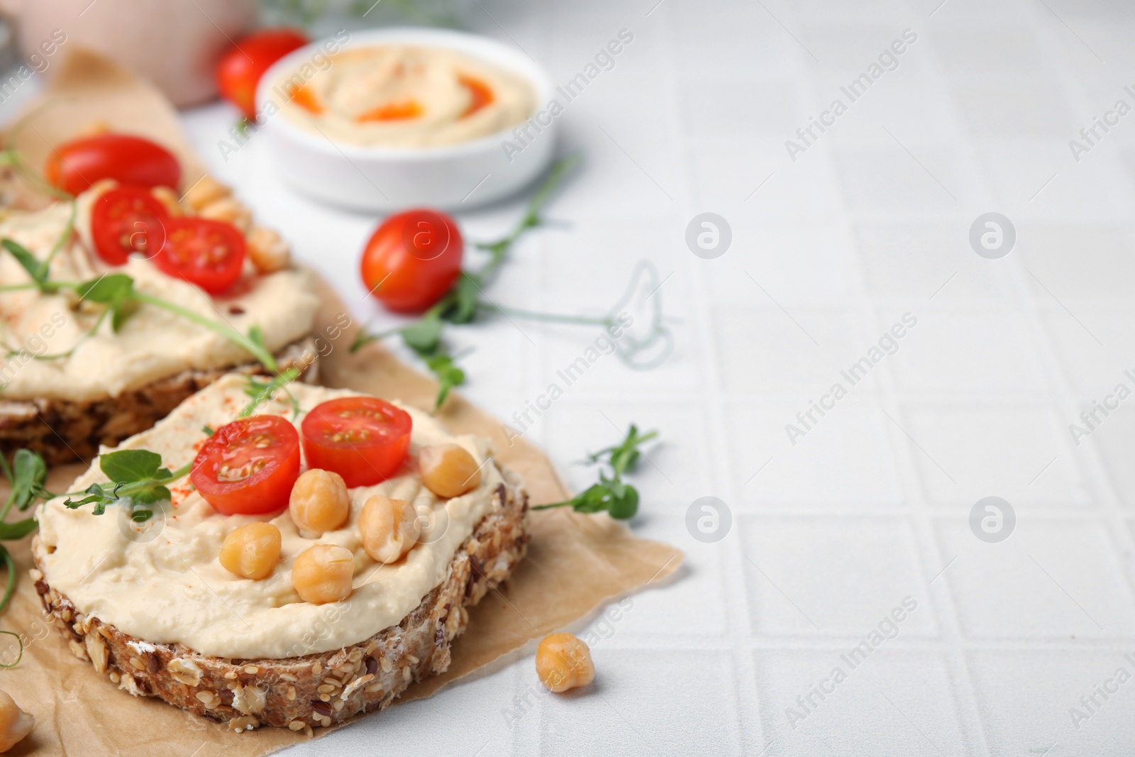 Photo of Delicious sandwiches with hummus and ingredients on white tiled table. Space for text
