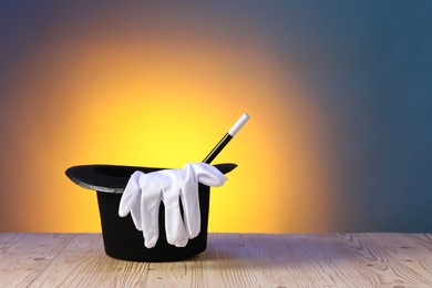 Photo of Magician's hat, wand and gloves on wooden table against color background, space for text