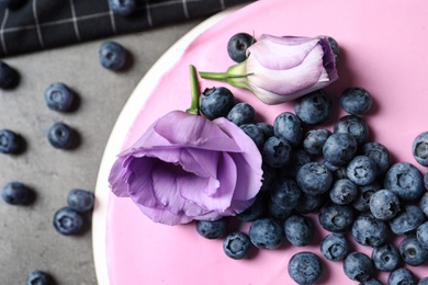 Tasty blueberry cake decorated with fresh flowers on grey table, closeup