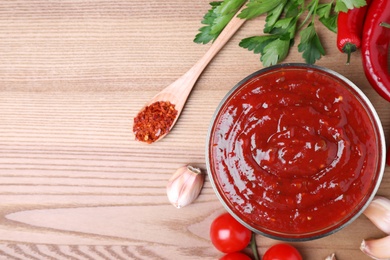 Photo of Bowl of hot chili sauce and ingredients on wooden background, flat lay. Space for text